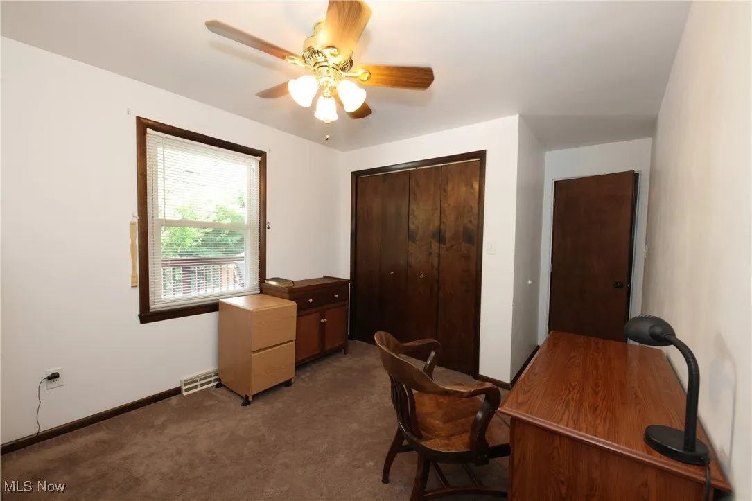 Carpeted office space featuring ceiling fan and baseboards