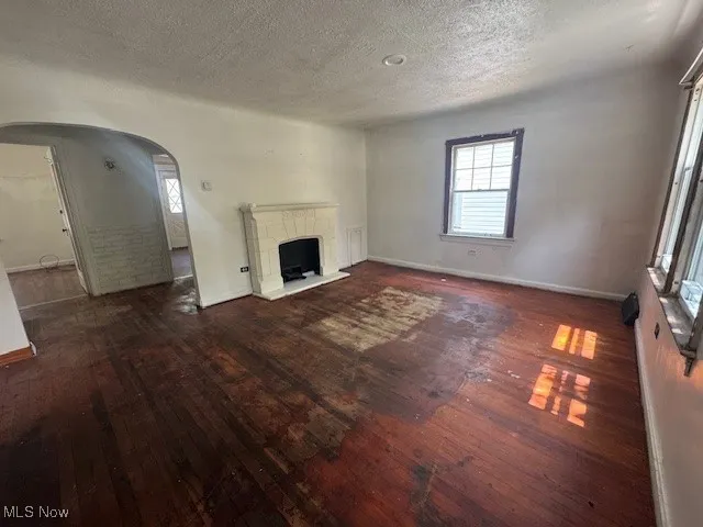 Unfurnished living room with wood-type flooring, a textured ceiling, a fireplace with raised hearth, and arched walkways