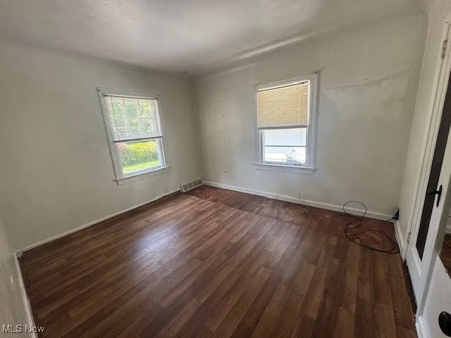 Spare room with dark wood-style flooring and baseboards