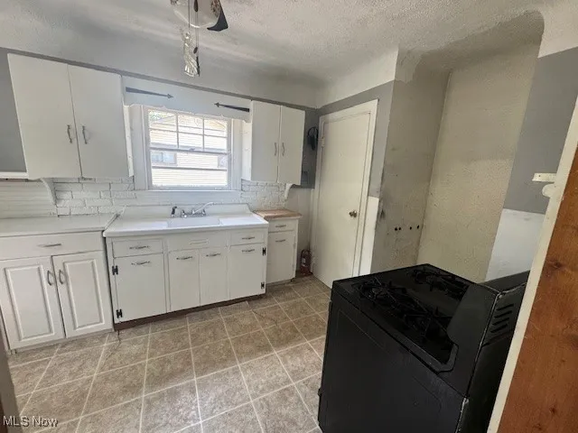 Kitchen featuring black range, tasteful backsplash, white cabinets, light countertops, and a textured ceiling
