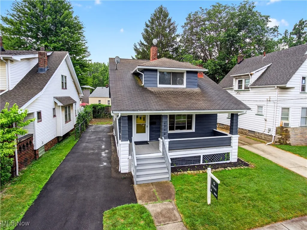 Bungalow-style home featuring driveway, covered porch, a front lawn, roof with shingles, and cooling unit