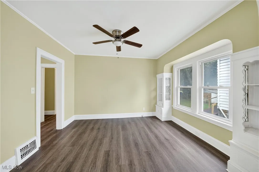 Spare room with ceiling fan, dark wood-style flooring, and crown molding