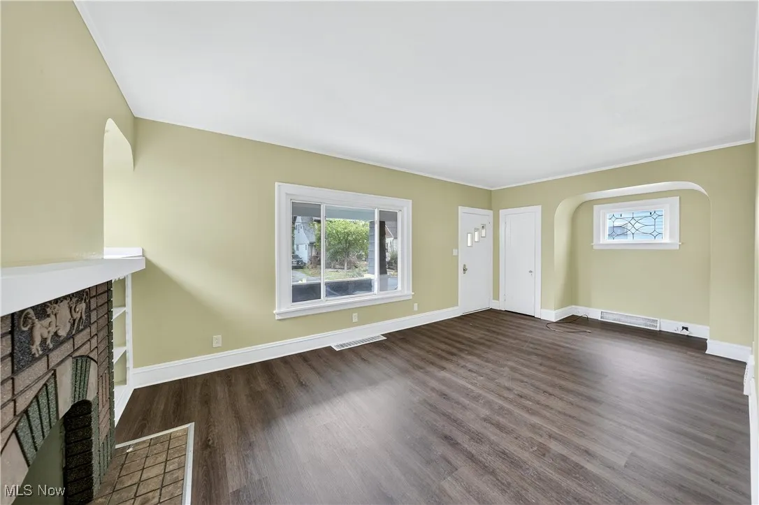 Unfurnished living room featuring healthy amount of natural light, dark wood finished floors, a fireplace, and arched walkways