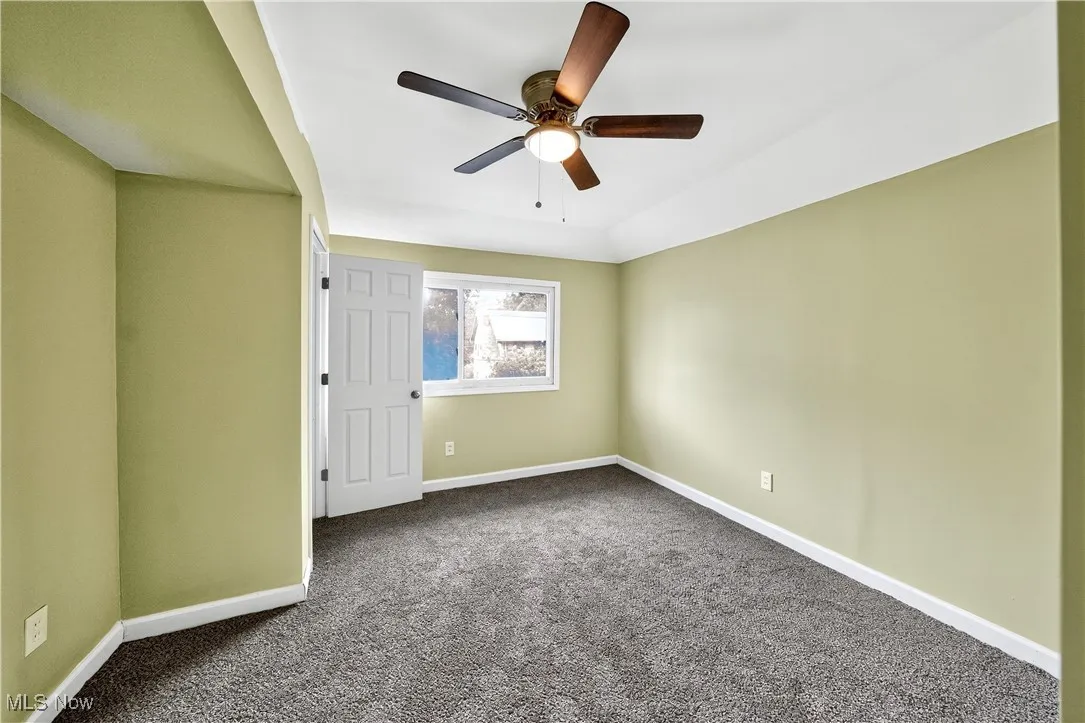 Empty room featuring dark carpet and a ceiling fan