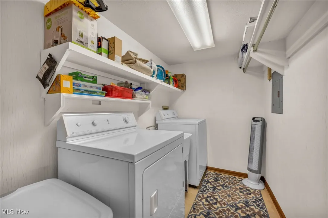 Washroom with independent washer and dryer, electric panel, and light tile patterned floors