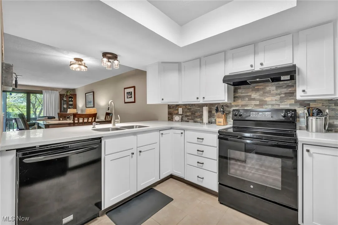 Kitchen featuring black appliances, under cabinet range hood, decorative backsplash, and light countertops