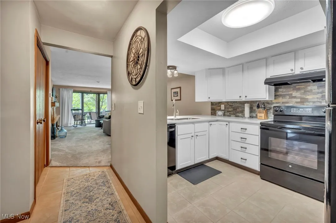Kitchen featuring electric range, under cabinet range hood, stainless steel dishwasher, white cabinets, and light countertops