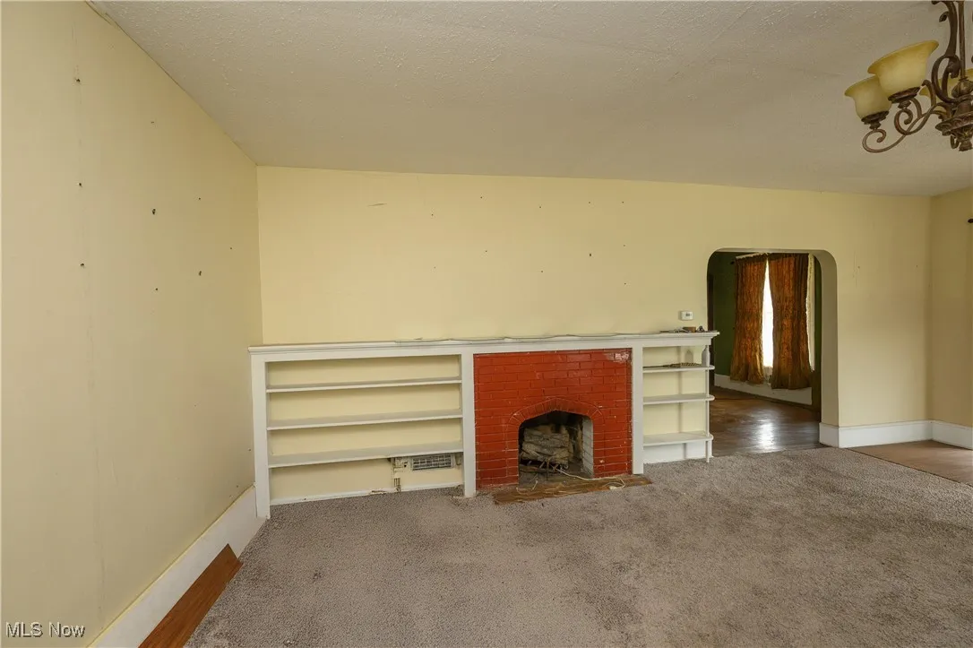 Unfurnished living room featuring carpet floors, arched walkways, a chandelier, and a brick fireplace