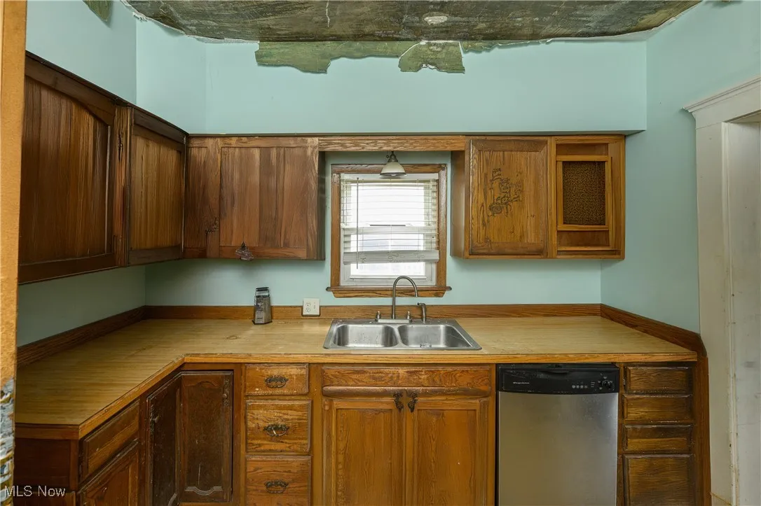 Kitchen with stainless steel dishwasher, light countertops, and brown cabinets