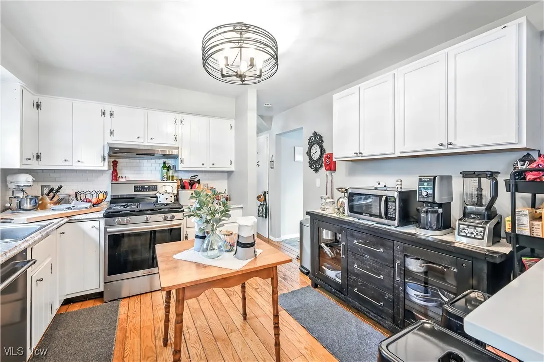 Kitchen featuring stainless steel appliances, light wood-type flooring, white cabinetry, light countertops, and under cabinet range hood