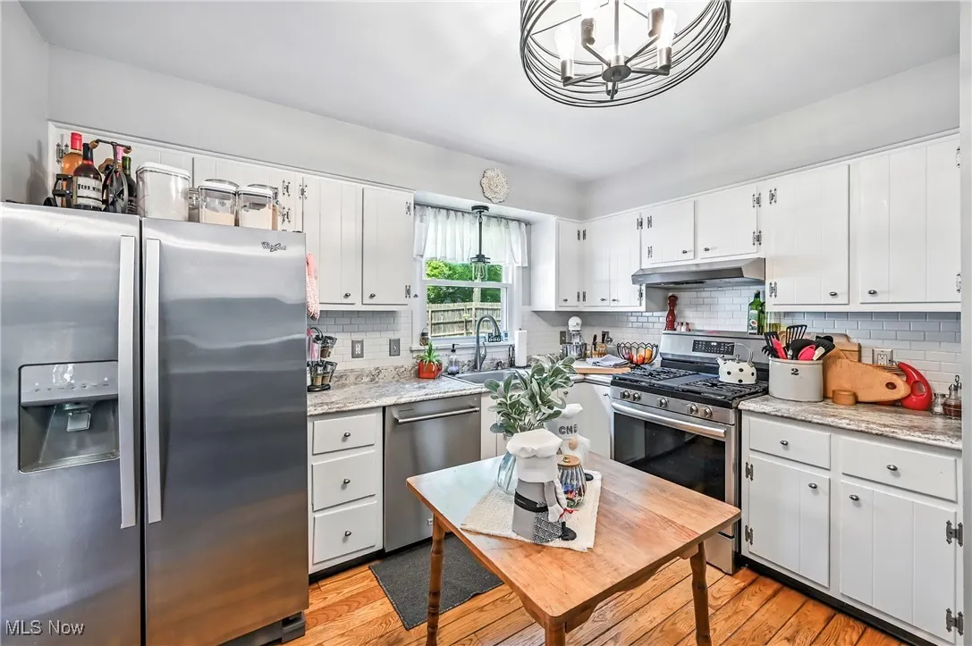 Kitchen with stainless steel appliances, light wood-type flooring, a chandelier, and under cabinet range hood