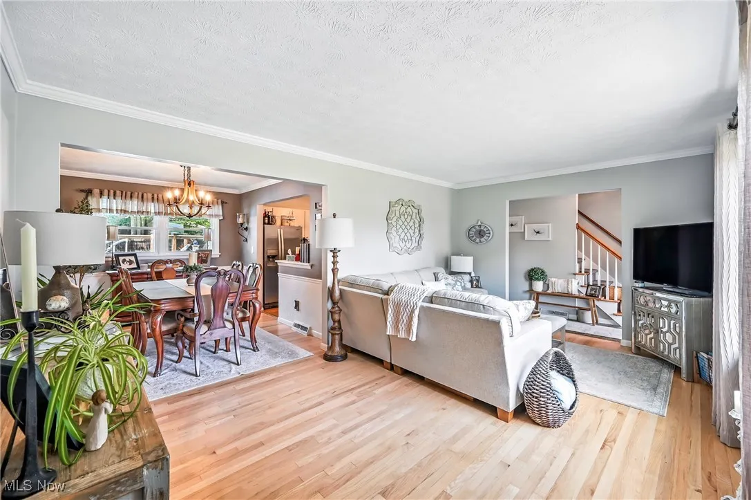 Living area with light wood-style flooring, a chandelier, stairway, ornamental molding, and a textured ceiling