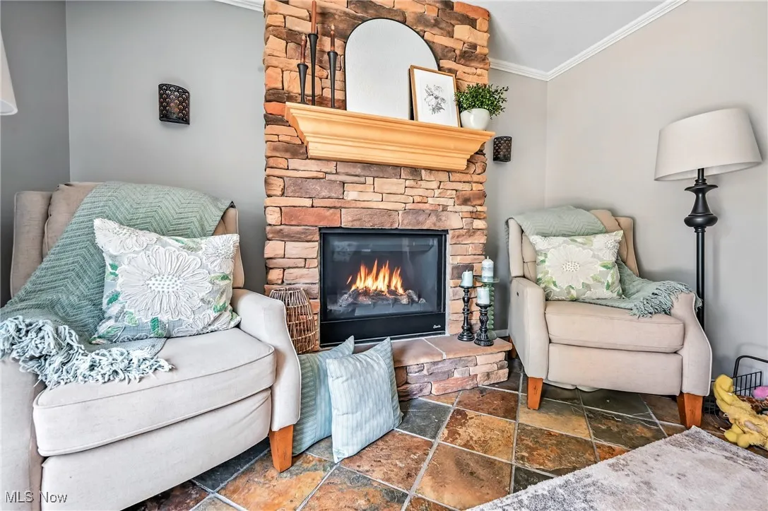 Living area with stone tile flooring, ornamental molding, and a stone fireplace