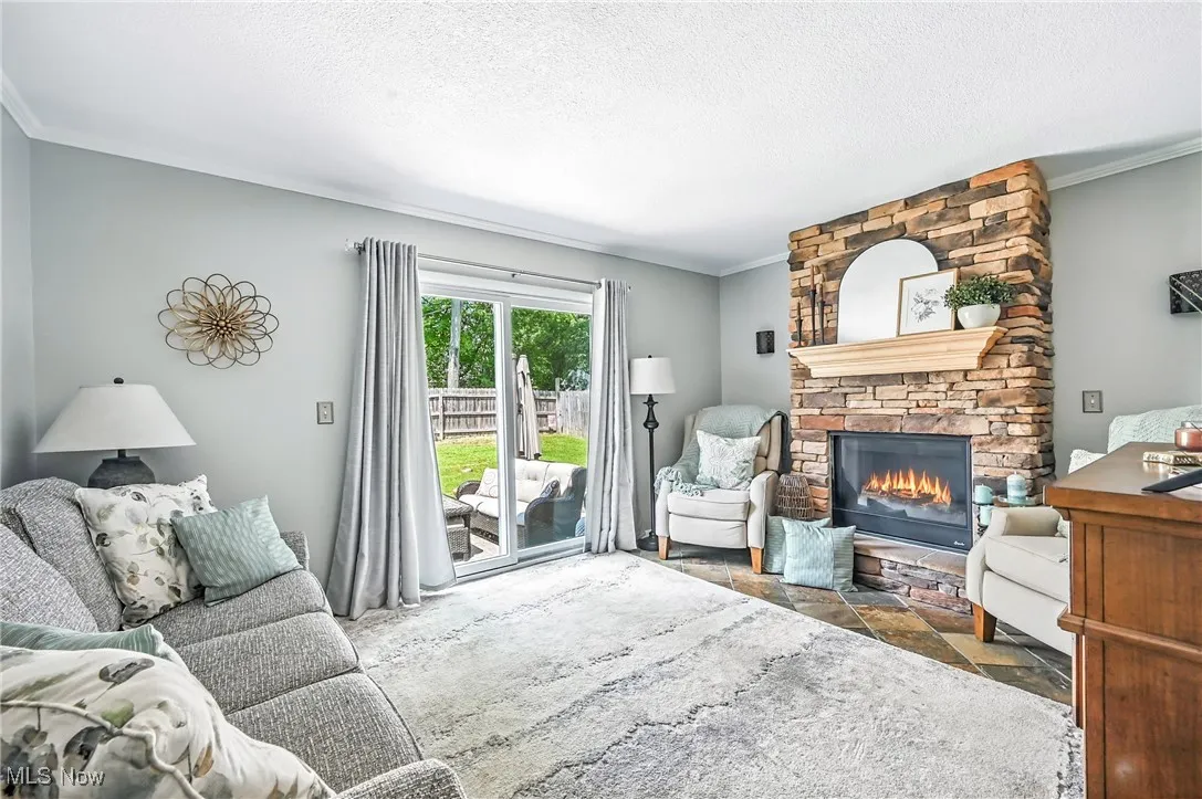 Living room with stone finish flooring, a fireplace, ornamental molding, and a textured ceiling