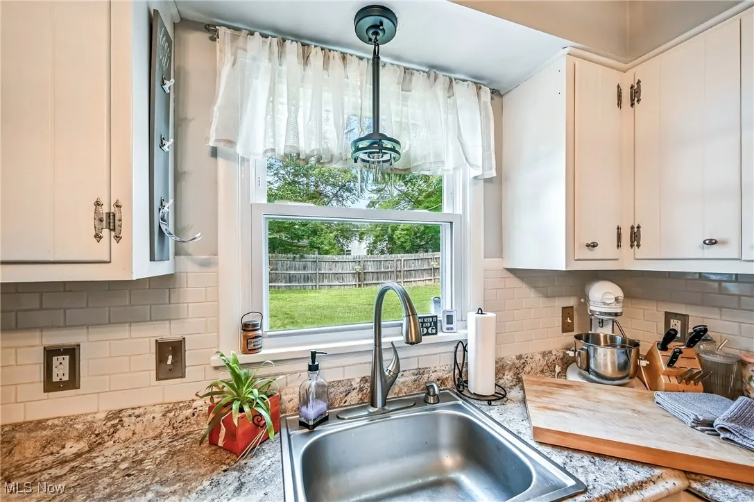 Kitchen featuring decorative backsplash, white cabinets, and hanging light fixtures