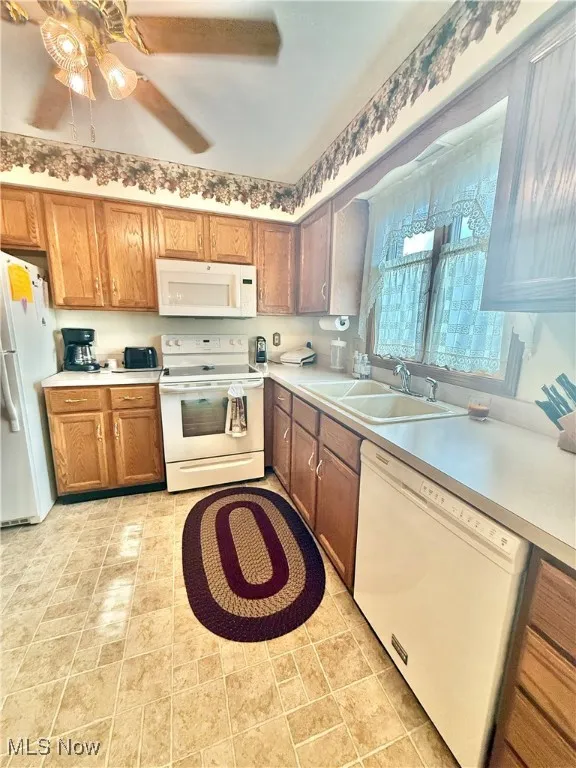Kitchen with white appliances, brown cabinetry, light countertops, and a ceiling fan