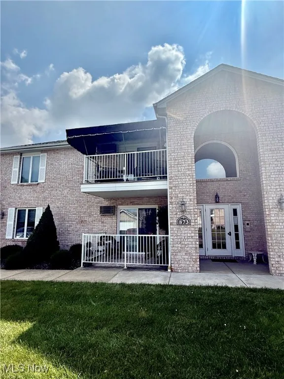 Back of house featuring brick siding, a balcony, a lawn, and a patio