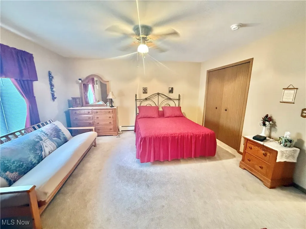 Bedroom featuring a baseboard radiator, carpet, a ceiling fan, and a closet