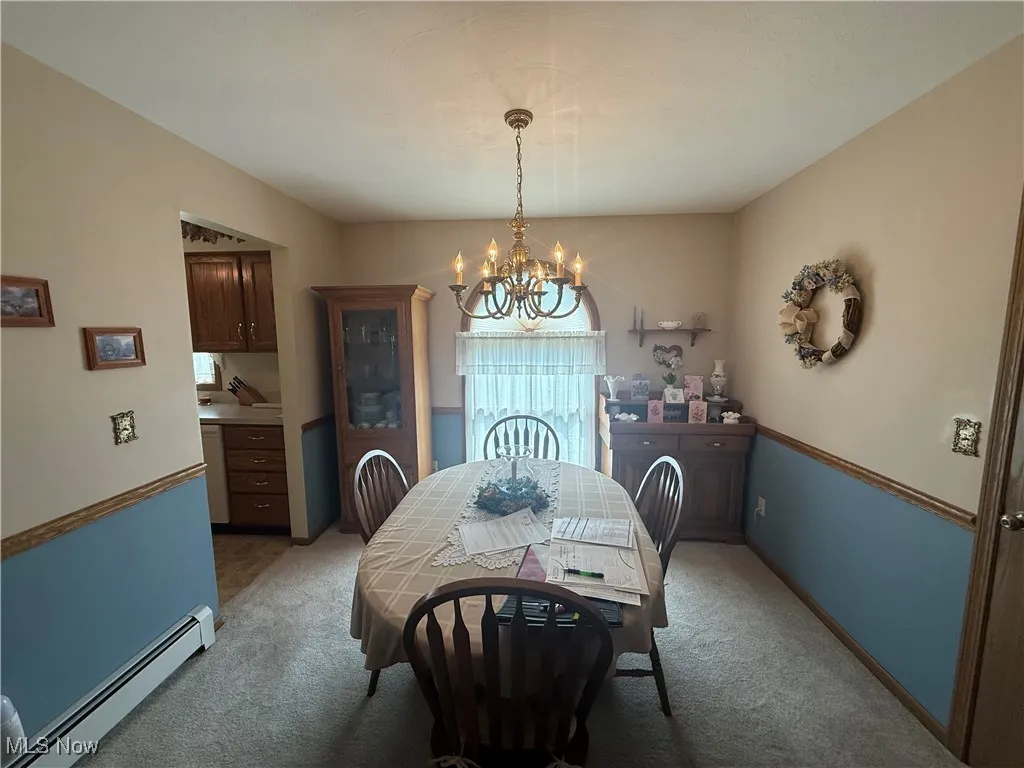 Dining area with a baseboard heating unit, a chandelier, and light carpet