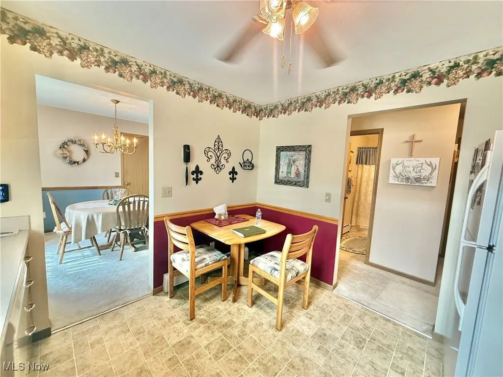Dining area with a ceiling fan, a chandelier, light carpet, and a wainscoted wall