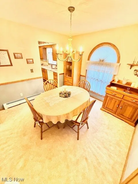 Dining area with baseboard heating, light colored carpet, and a chandelier