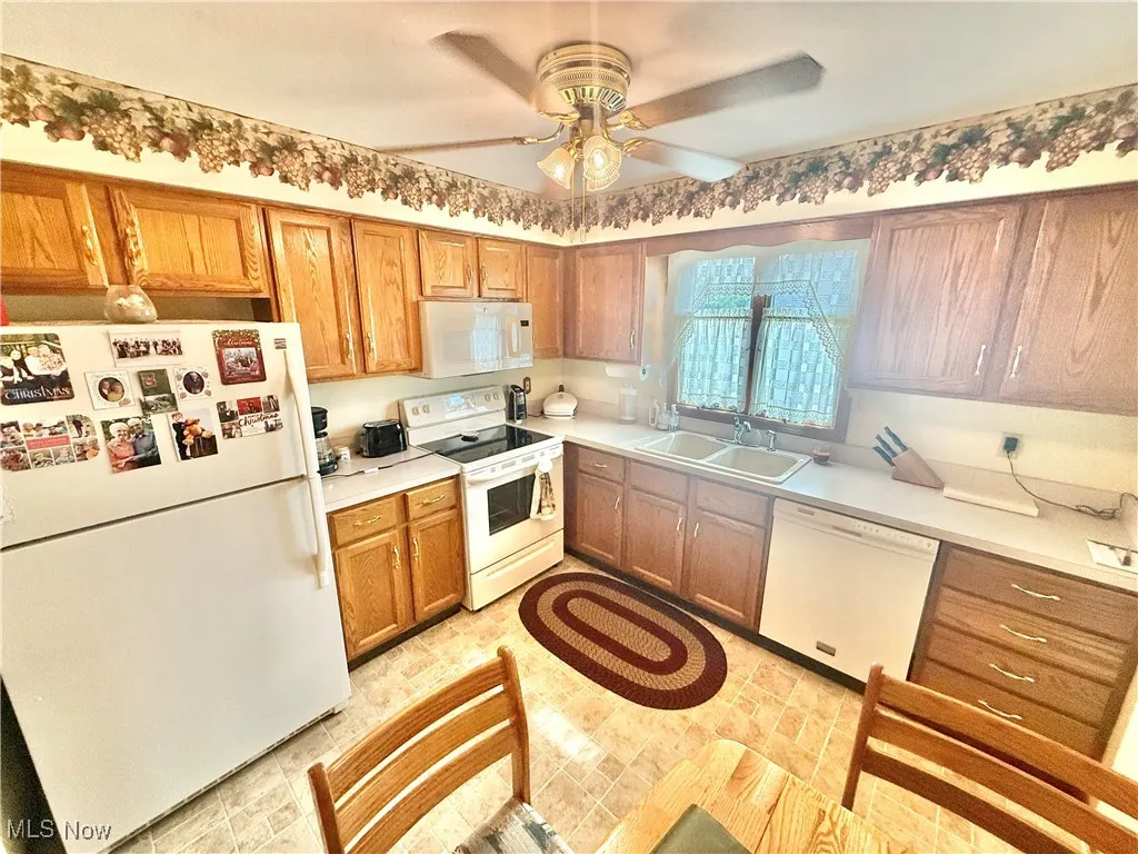 Kitchen featuring white appliances, a ceiling fan, brown cabinetry, and light countertops