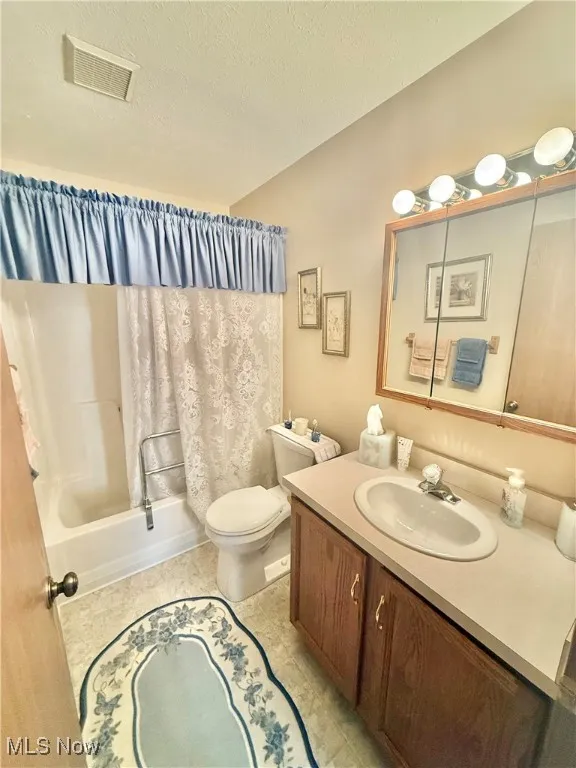 Bathroom featuring vanity, shower / bath combo with shower curtain, and a textured ceiling