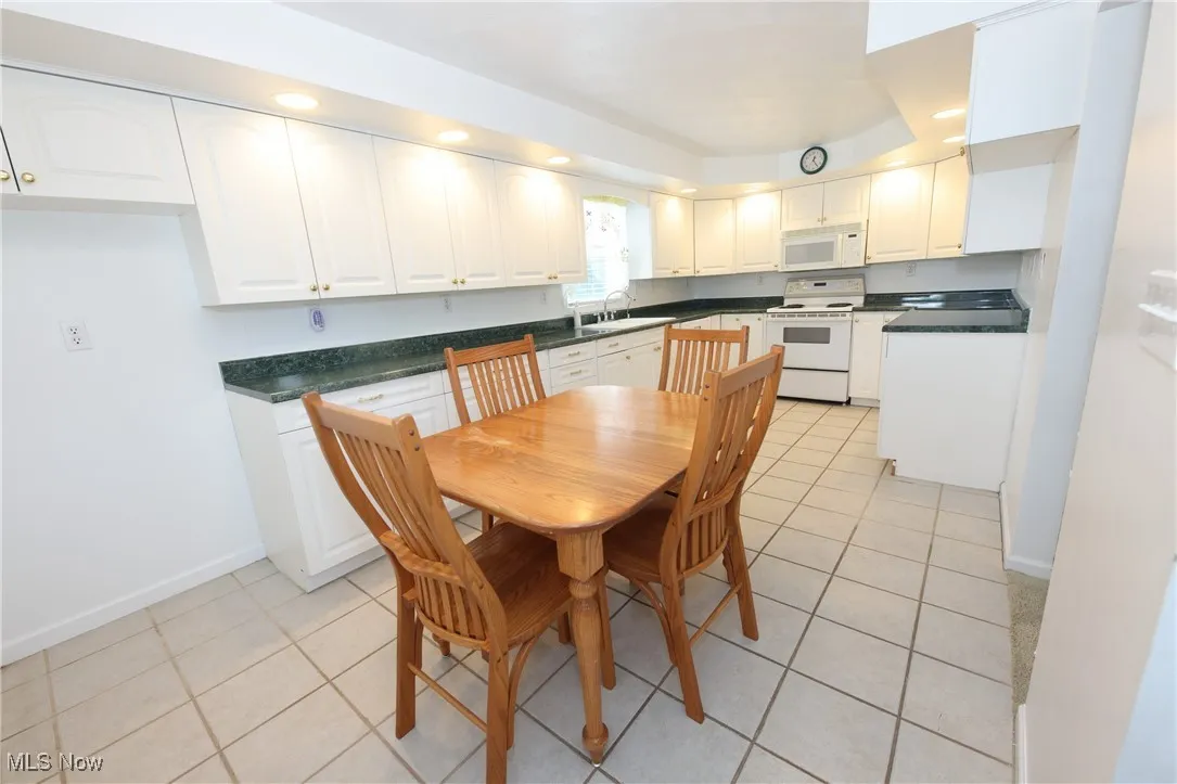 Kitchen featuring white appliances, light tile patterned floors, dark countertops, white cabinetry, and recessed lighting