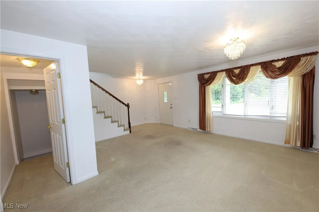 Unfurnished living room with stairs and light colored carpet
