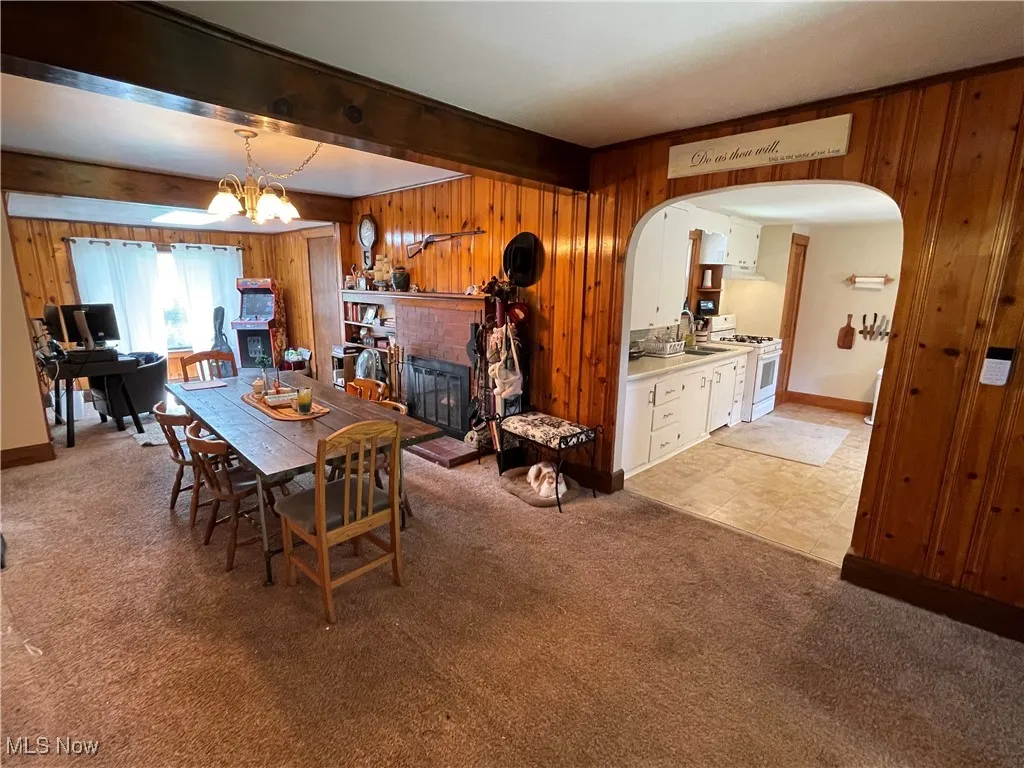 Dining area with wood walls, arched walkways, light carpet, a fireplace, and beam ceiling
