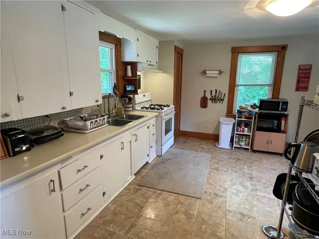 Kitchen with white gas range oven, stainless steel microwave, under cabinet range hood, tasteful backsplash, and light countertops