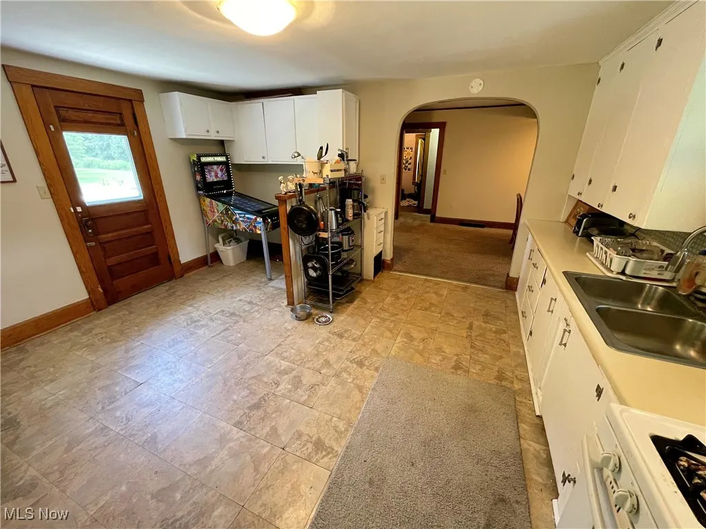 Kitchen featuring arched walkways, white cabinets, and light countertops