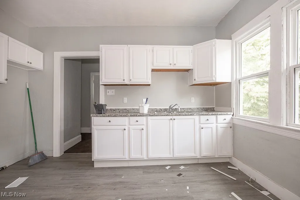 Kitchen with plenty of natural light, white cabinetry, light wood-style floors, and light stone countertops