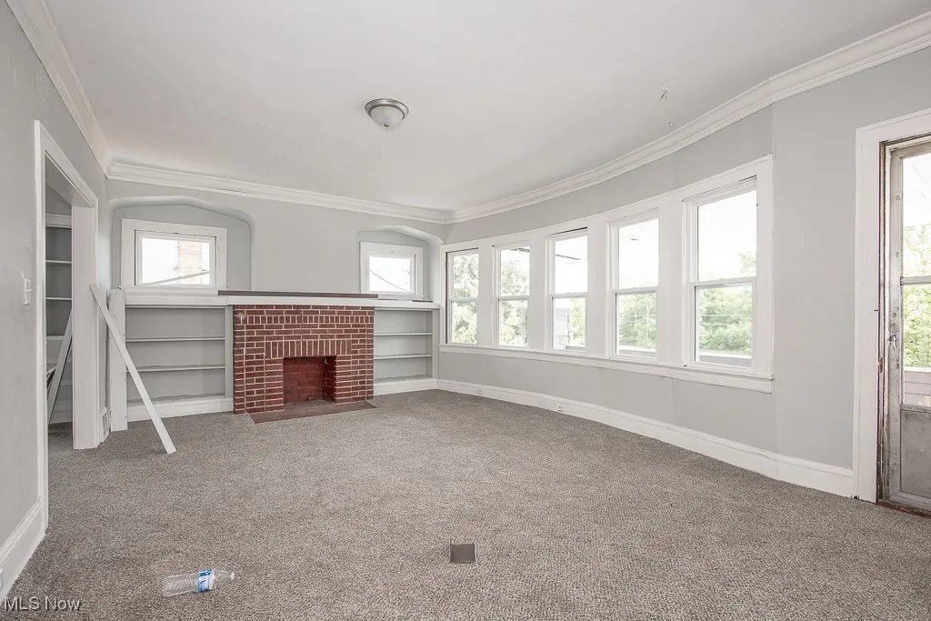 Unfurnished living room featuring crown molding, plenty of natural light, carpet flooring, and a brick fireplace