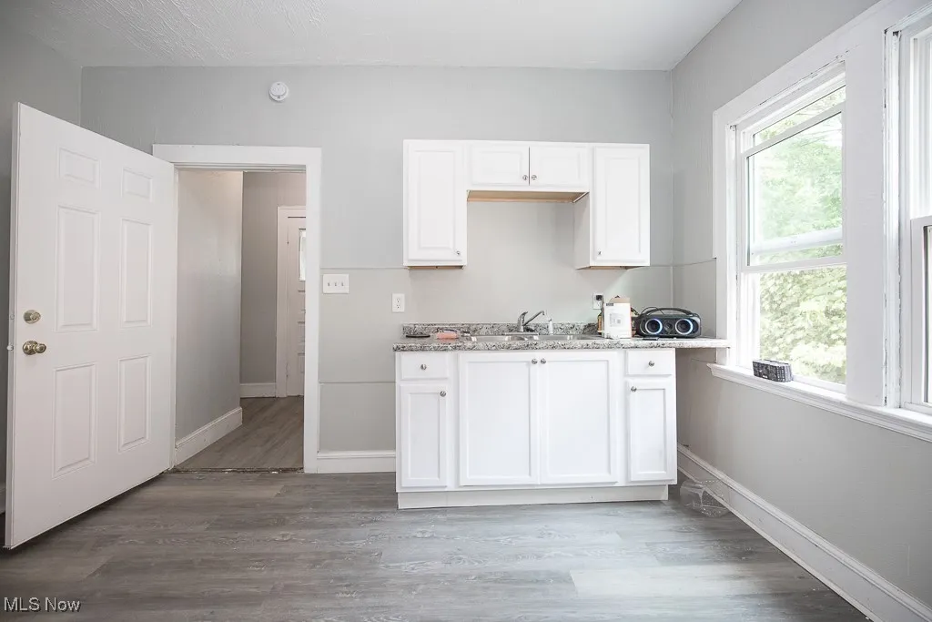Kitchen featuring white cabinets, light stone counters, and wood finished floors
