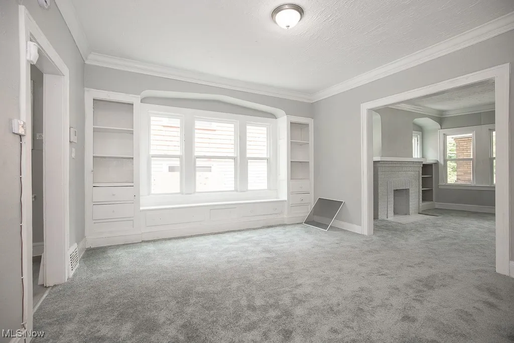Unfurnished living room featuring carpet flooring, ornamental molding, a brick fireplace, and a textured ceiling