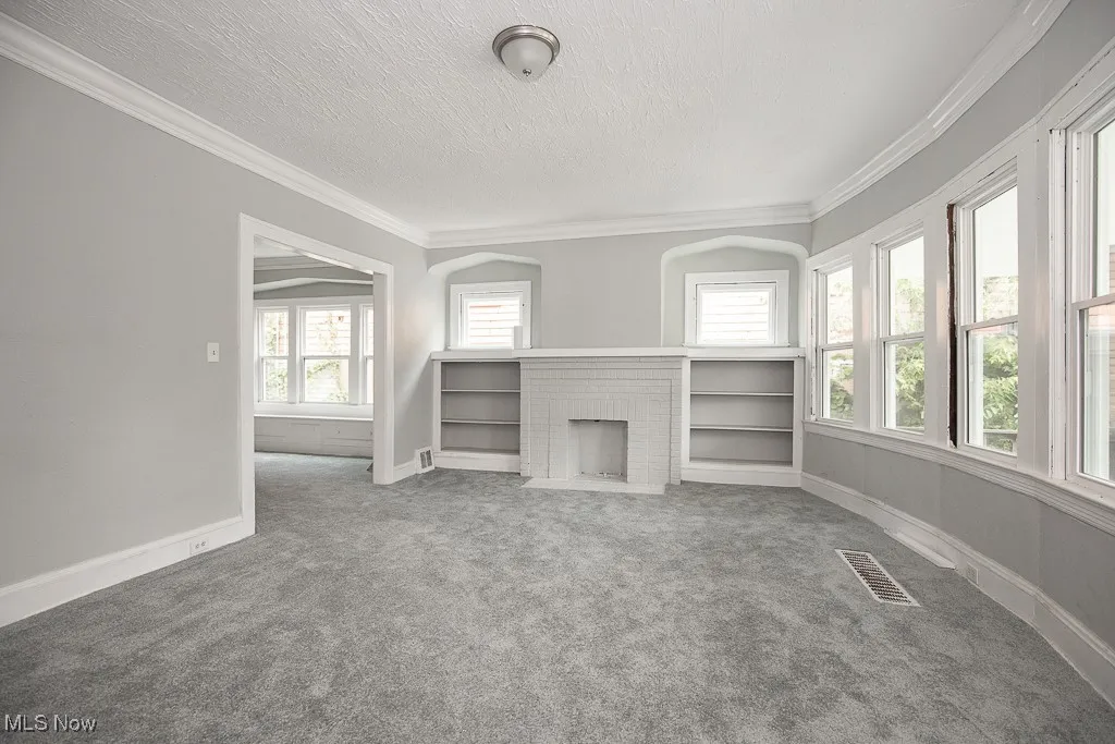 Unfurnished living room featuring carpet floors, a fireplace, crown molding, and a textured ceiling