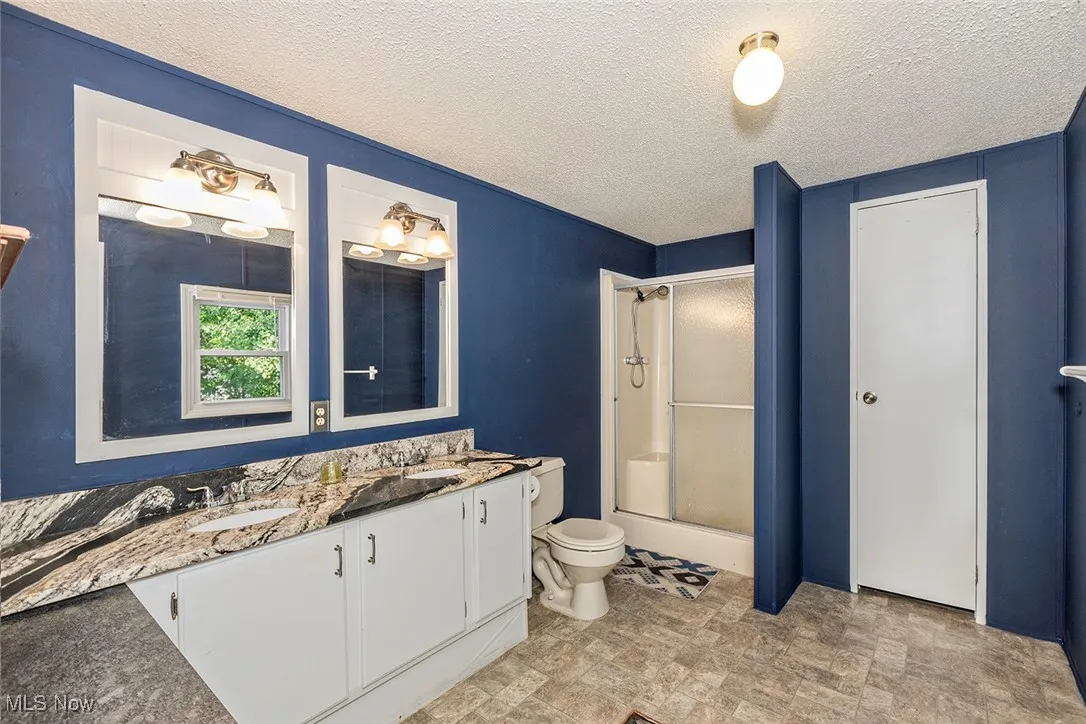 Bathroom featuring a shower with door, double vanity, and a textured ceiling