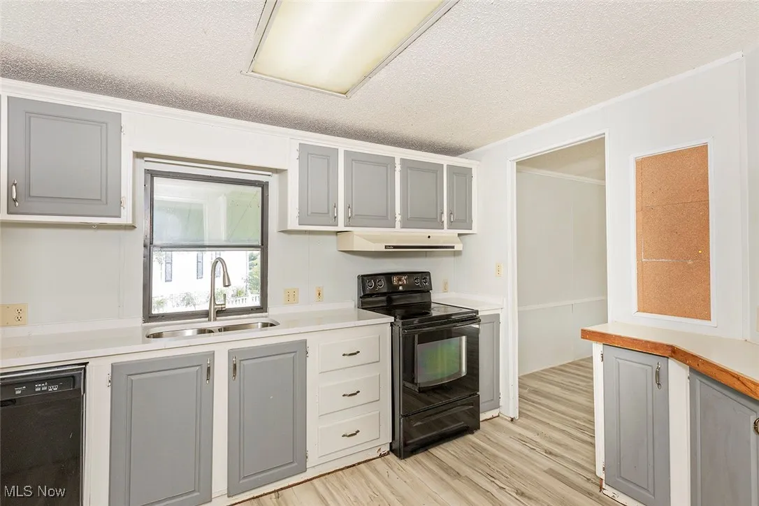 Kitchen featuring black appliances, under cabinet range hood, a textured ceiling, gray cabinetry, and light wood-style floors