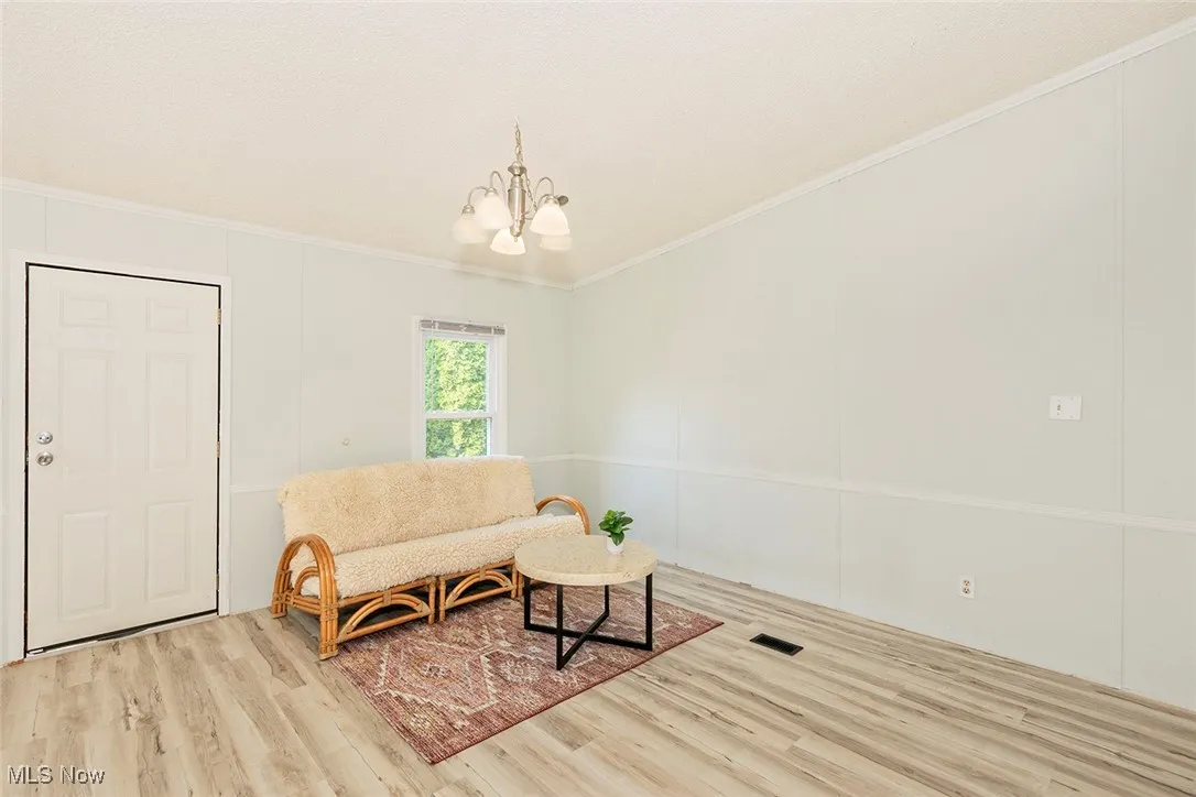 Sitting room with a chandelier, wood finished floors, and ornamental molding