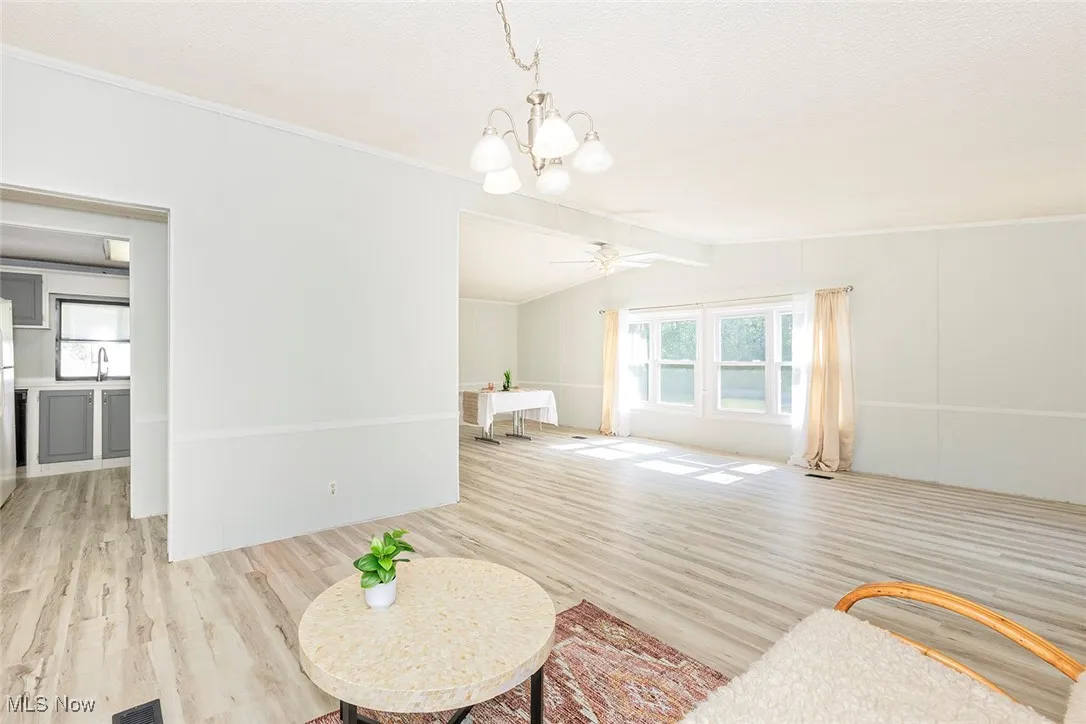 Living room featuring wood finished floors, a ceiling fan, a chandelier, and crown molding