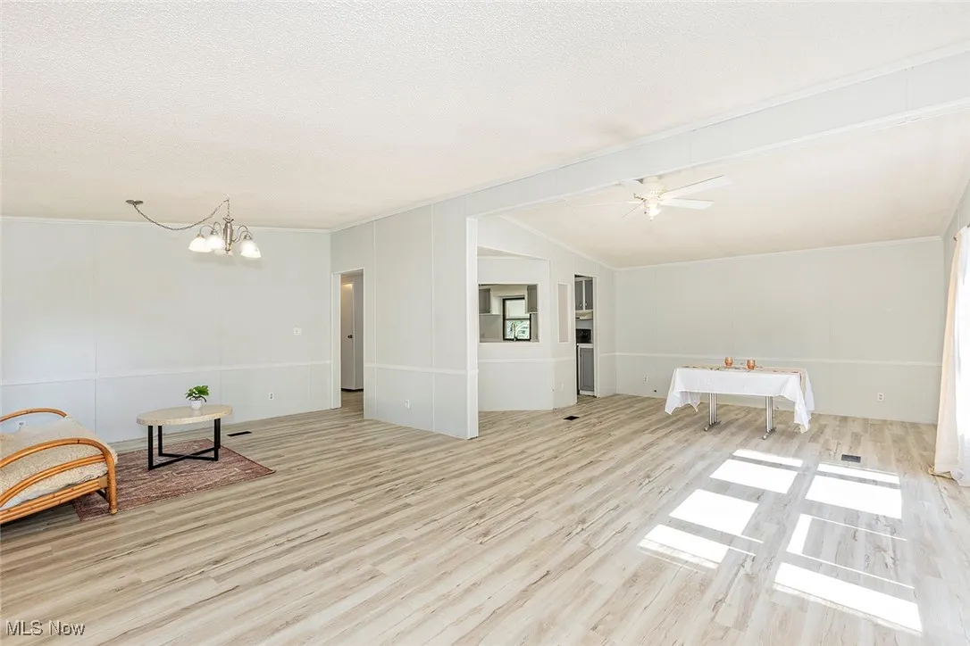 Unfurnished room featuring wood finished floors, a chandelier, lofted ceiling, ceiling fan, and a textured ceiling