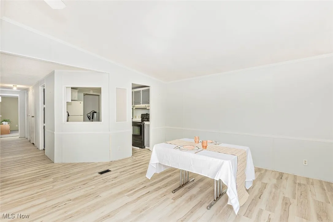 Dining room with light wood-style floors, crown molding, and lofted ceiling