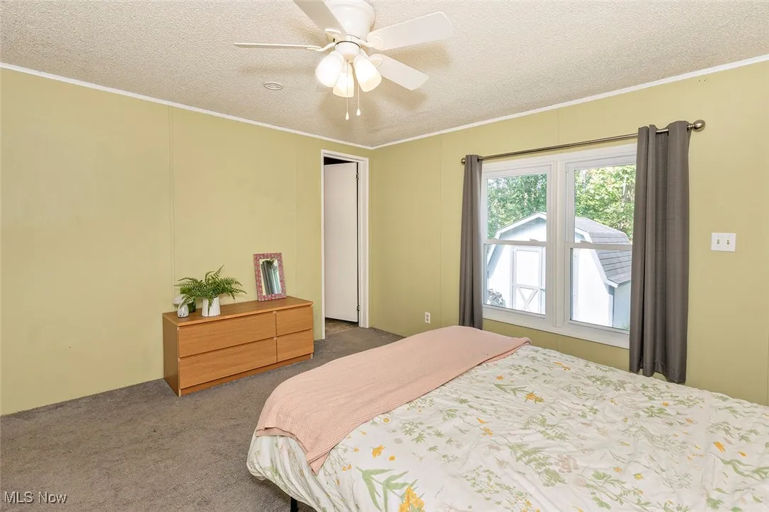 Bedroom featuring carpet, a textured ceiling, ornamental molding, and a ceiling fan