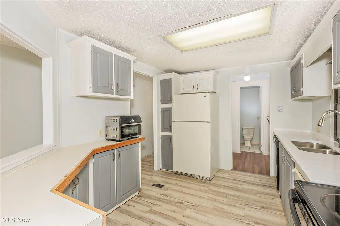 Kitchen with freestanding refrigerator, light countertops, light wood-type flooring, stove, and a textured ceiling