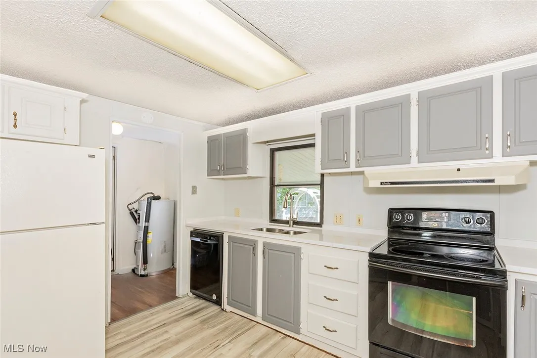 Kitchen with black appliances, range hood, light wood finished floors, light countertops, and a textured ceiling