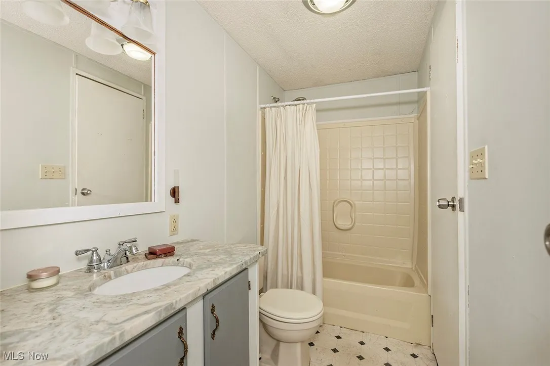 Full bath with vanity, shower / bath combo, a textured ceiling, and tile patterned floors
