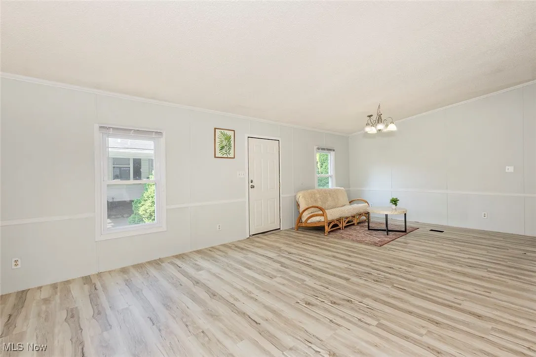 Living area with a chandelier, wood finished floors, and ornamental molding