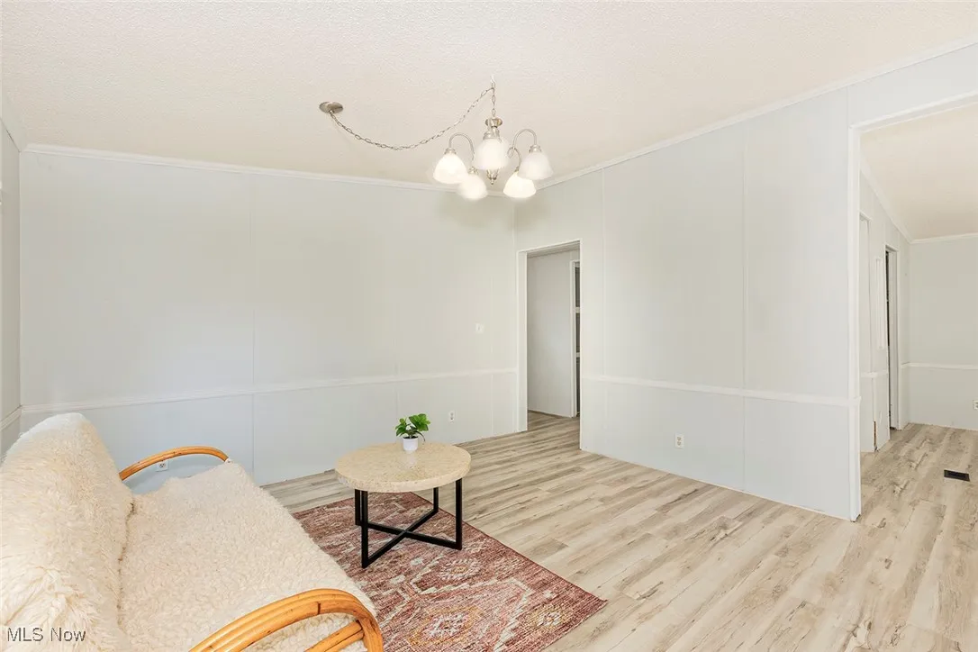 Living area with ornamental molding, a chandelier, and wood finished floors
