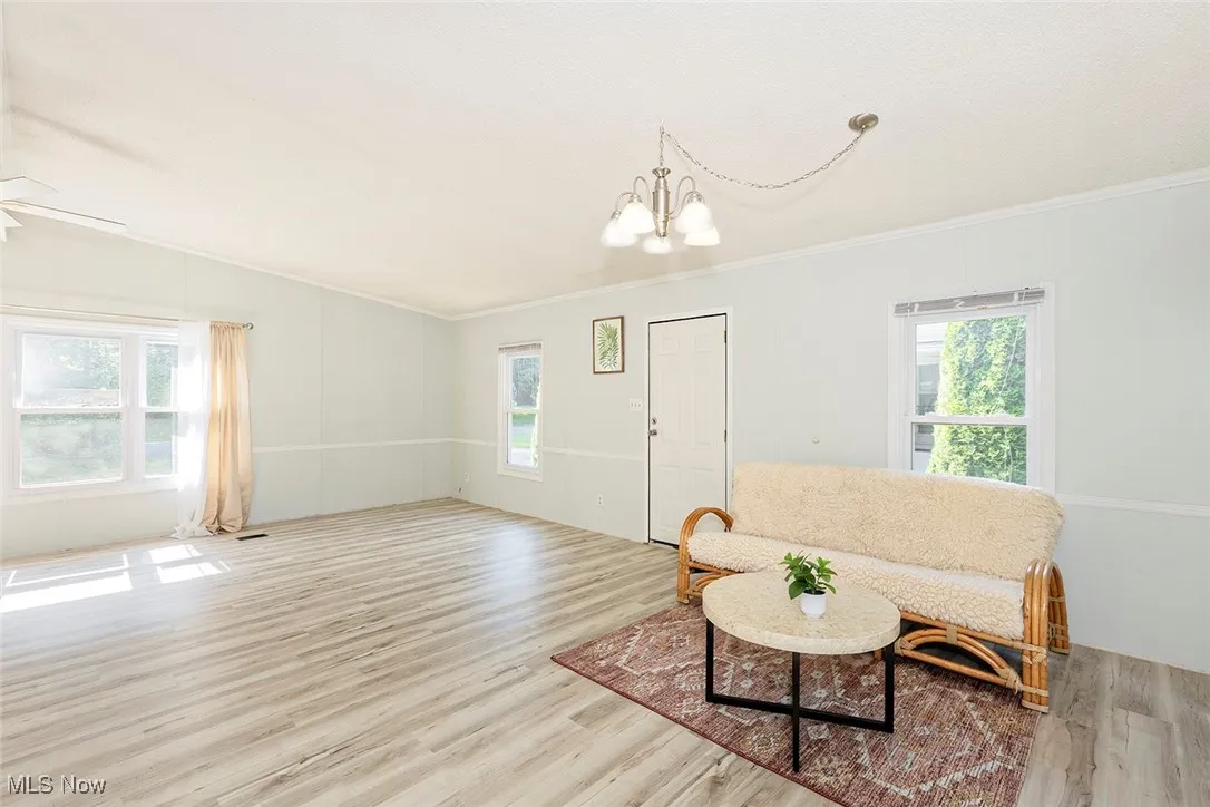 Living room with a chandelier, wood finished floors, plenty of natural light, and ornamental molding